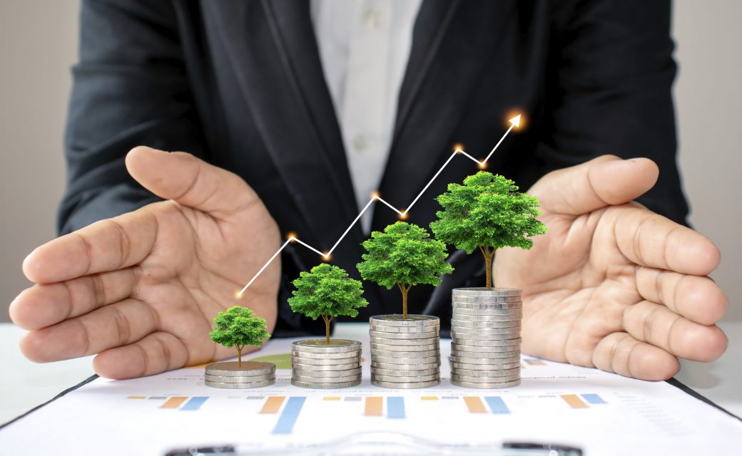 The green tree that is growing on coins increases in various forms, including the hands of business people that surround the pile of coins and the rising arrow graph. The concept of business growth.